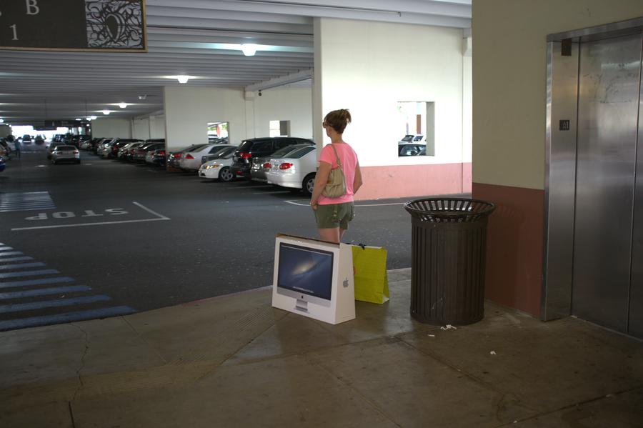 A woman waiting in a parking structure with a new Mac computer