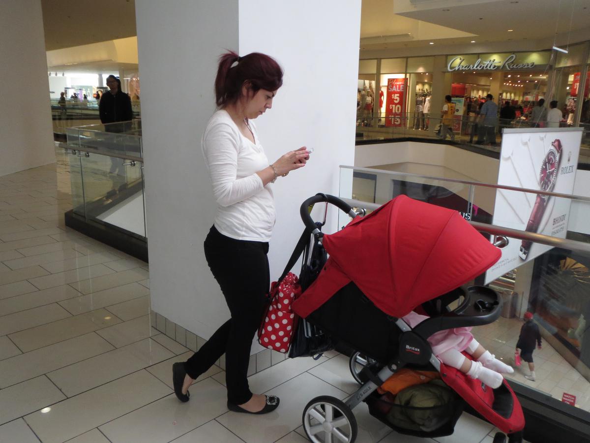 Woman with a stroller looking at her phone as she waits