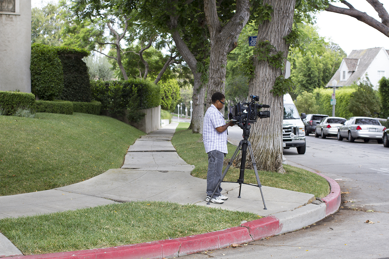 Camera person sets up a large news camera on a tree-lined street